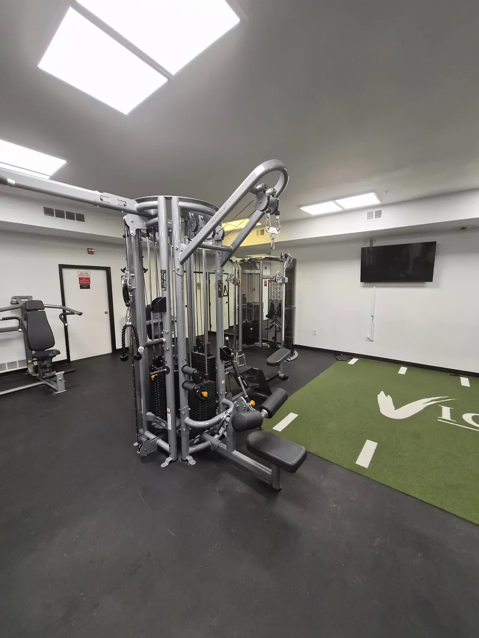 Weight-training equipment beside an indoor turf area in a fitness room